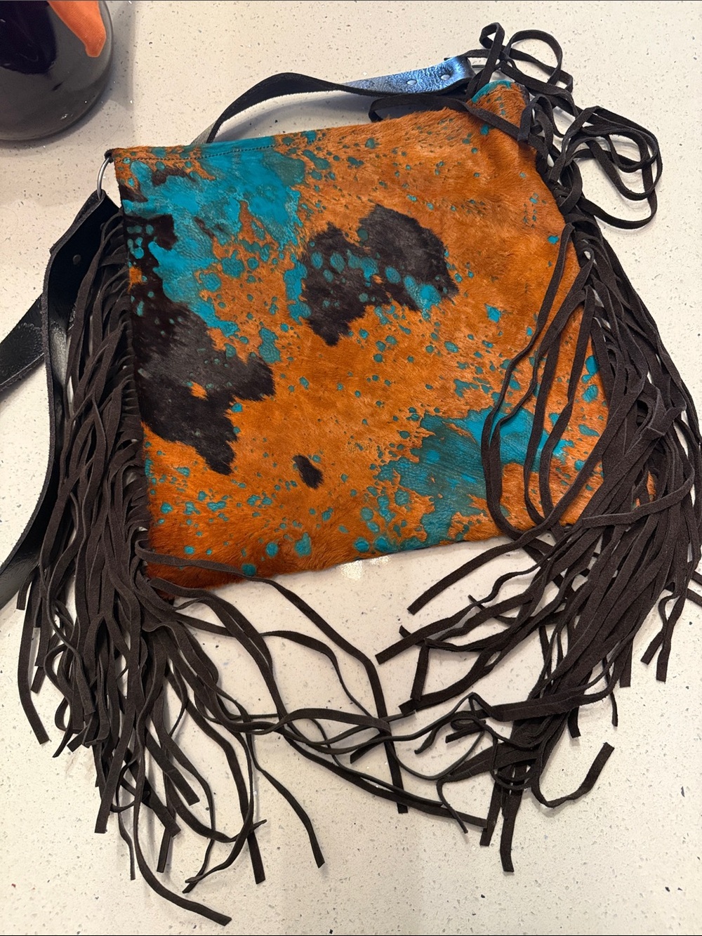 Stylish fringe crossbody featuring a black and brown haircalf with teal accents